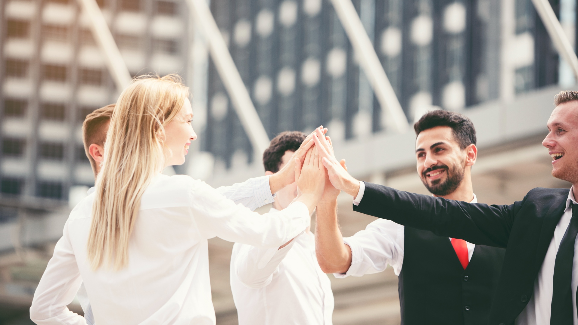 Um grupo de quatro profissionais de negócios, dois homens e duas mulheres, estão de pé ao ar livre em frente a um edifício moderno. Eles estão sorrindo e dando um high-five como uma equipe. Vestidos em trajes formais, eles parecem estar celebrando ou compartilhando um momento de sucesso, verdadeiramente incorporando o espírito dos business angels o que é. - Efacont