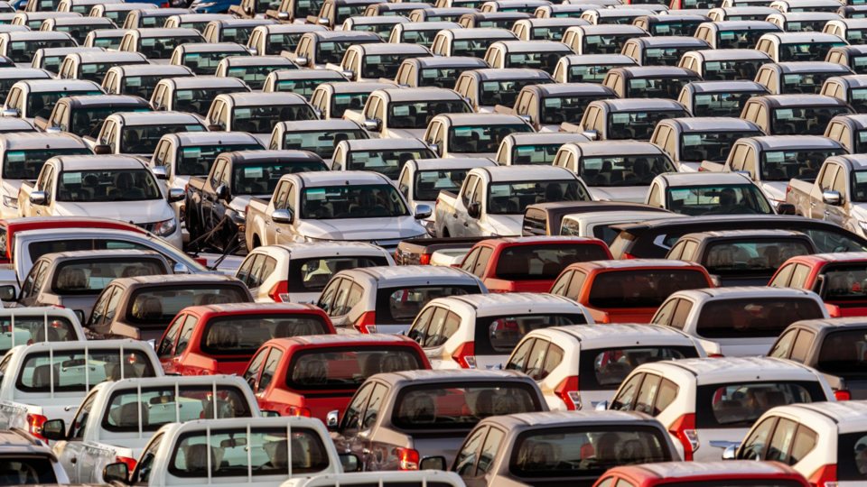 Em um grande estacionamento em Portugal, fileiras de veículos estão bem apinhadas e, em sua maioria, brancas, com algumas vermelhas espalhadas por toda parte. Voltados para a mesma direção e se aquecendo sob a luz natural do dia de 2024, esses carros parecem preparados para embarque ou venda. - Efacont